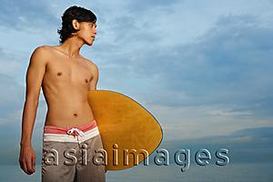 Asia Images Group - Young man holding skimboard, looking away
