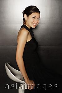 Asia Images Group - Young woman in black dress sitting on stool, smiling at camera