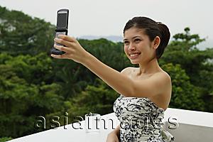 Asia Images Group - Young woman in floral dress, standing on balcony, using mobile phone to take a picture