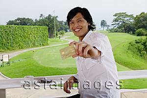 Asia Images Group - Man holding credit card, smiling at camera, golf course behind him
