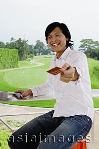 Asia Images Group - Man holding credit card, towards camera, golf course behind him