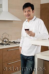 Asia Images Group - Man standing in kitchen, holding wine glass, looking at camera