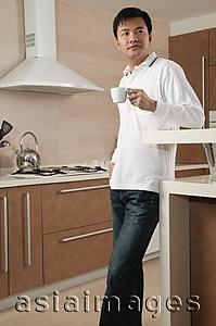 Asia Images Group - Man standing in kitchen, holding cup, looking away