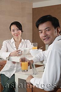 Asia Images Group - Couple in kitchen having breakfast, looking at camera