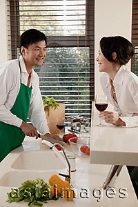Asia Images Group - Couple in kitchen, man chopping vegetables, woman leaning on counter with wine glass