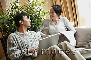 Asia Images Group - Couple in living room, man with laptop, woman holding magazine
