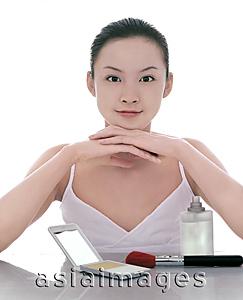 Asia Images Group - Young woman looking at camera, make-up on the table around her