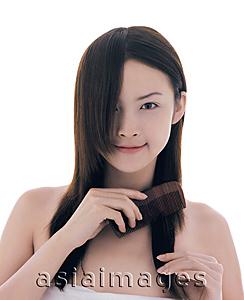 Asia Images Group - Young woman combing her hair, looking at camera