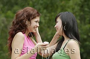 Asia Images Group - Two teenage girls listening to MP3 player, smiling