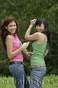 Asia Images Group - Two teenage girls listening to MP3 player, dancing and smiling at camera