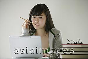 Asia Images Group - Young woman with laptop, biting pencil, looking at camera