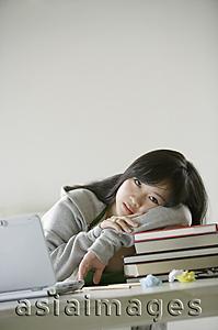 Asia Images Group - Young woman resting on stack of books, looking at camera