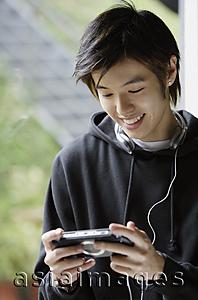 Asia Images Group - Young man looking at MP3 player, smiling