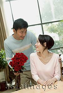 Asia Images Group - Couple in loving room, man holding bouquet of flowers, woman turning to look at him