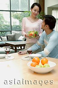 Asia Images Group - Couple at home, man sitting at dining table, woman standing next to him holding bowl of salad