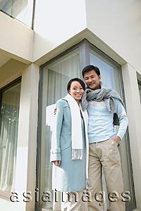 Asia Images Group - Couple standing outside house, smiling at camera