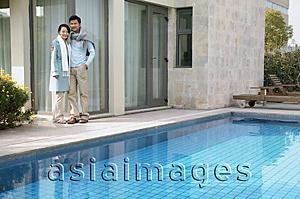 Asia Images Group - Couple standing outside house, next to swimming pool