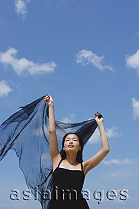 Asia Images Group - Woman in black dress, eyes closed, holding scarf in air
