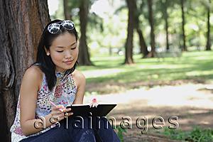 Asia Images Group - Young woman sitting outdoors, writing in notebook