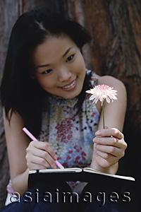 Asia Images Group - Young woman holding flower, writing in notebook