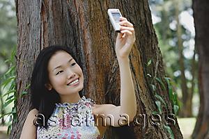 Asia Images Group - Young woman outdoors, taking a photograph of herself with mobile phone camera