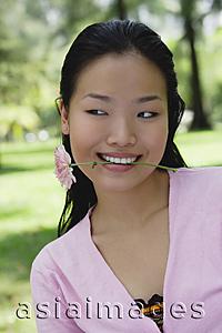 Asia Images Group - Young woman biting flower stalk, head shot