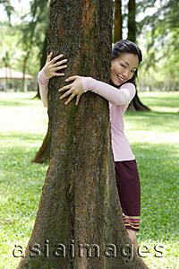 Asia Images Group - Young woman with arms around a tree