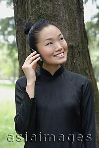Asia Images Group - Young woman in traditional Chinese costume, standing next to tree, using mobile phone