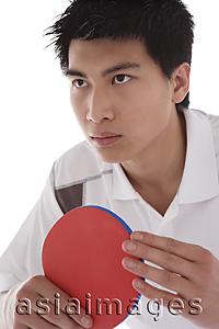 Asia Images Group - Young man holding table tennis paddle, looking away