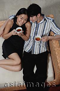 Asia Images Group - Couple sitting on sofa, holding cups of tea