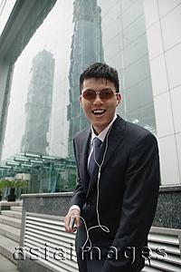 Asia Images Group - Businessman listening to MP3 player, smiling at camera
