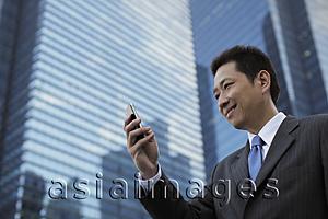 Asia Images Group - Mature man looking at a phone in front of a modern building and smiling