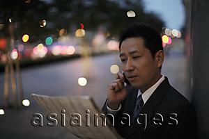 Asia Images Group - Mature man looking at newspaper and talking on the phone on the street