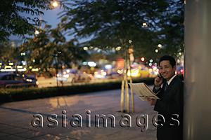 Asia Images Group - mature man holding a newspaper and talking on the phone in the evening