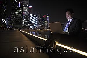 Asia Images Group - Mature man working on his laptop at night, buildings in background