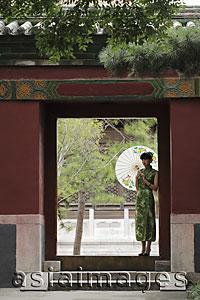 Asia Images Group - Young woman wearing Chinese traditional dress standing in doorway holding an umbrella