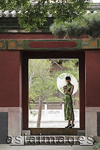Asia Images Group - Young woman wearing Chinese traditional dress standing in a doorway holding an umbrella