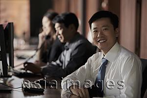 Asia Images Group - Young man in tie smiling, people working in background