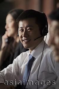 Asia Images Group - Young man wearing a head set smiling, background people