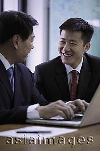 Asia Images Group - Businessmen smiling at each other while working on laptop