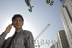 Asia Images Group - Young man talking on phone in front of construction site
