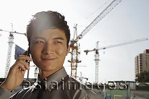 Asia Images Group - Young man with phone smiling, cranes in background
