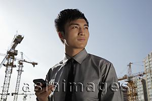 Asia Images Group - Young man holding phone, construction background