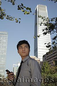 Asia Images Group - Young man holding phone standing in front of buildings, China