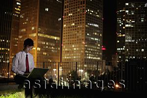 Asia Images Group - Young man working on laptop at night, with buildings in the background. Beijing, China