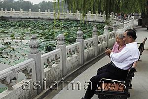 Asia Images Group - Older couple sitting on park bench looking at phone