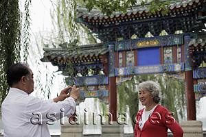 Asia Images Group - Older couple taking photos in front of traditional Chinese gate