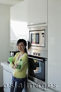 Asia Images Group - Young woman standing in kitchen smiling with arms folded