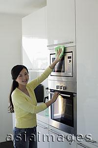 Asia Images Group - Young woman cleaning kitchen and smiling