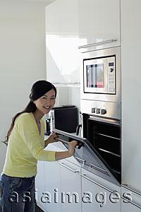 Asia Images Group - Young woman opening oven door and smiling